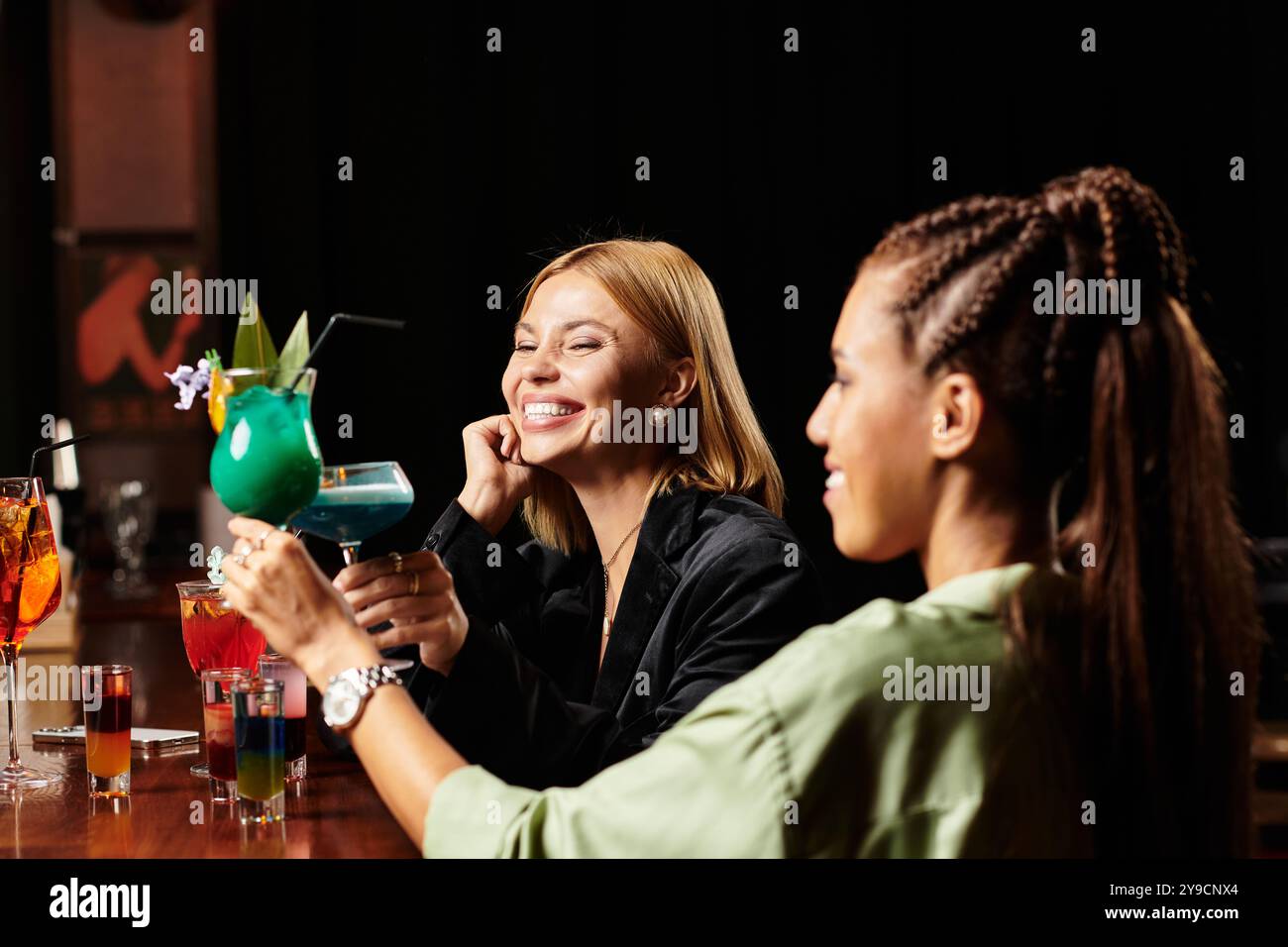 Zwei junge Profis genießen bunte Cocktails und Lachen während einer Firmenfeier. Stockfoto