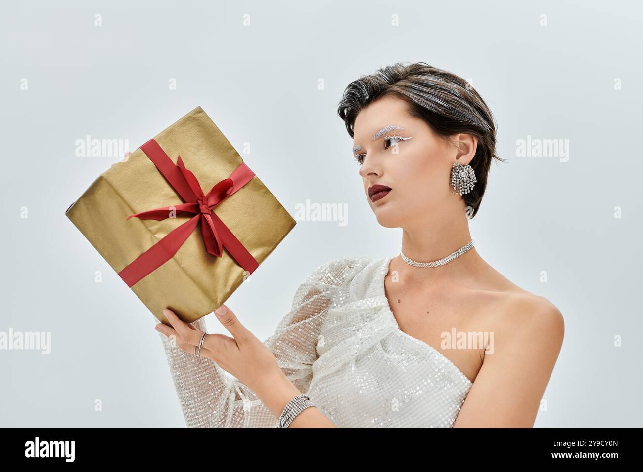 Eine wunderschön gekleidete Frau schaut auf ein schickes Geschenk, umgeben von einem gemütlichen Winterambiente. Stockfoto