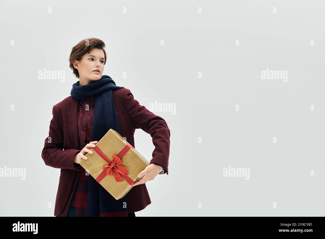 Eine stilvolle Frau in satten Winterfarben präsentiert ein üppig gewickeltes Geschenk mit Sorgfalt. Stockfoto