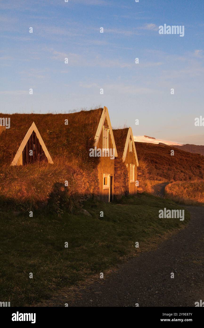 Charmante Rasenhäuser sonnen sich im goldenen Sonnenuntergangslicht, eingebettet in eine ruhige isländische Landschaft mit einem gewundenen Pfad, der in die Landschaft führt. Stockfoto