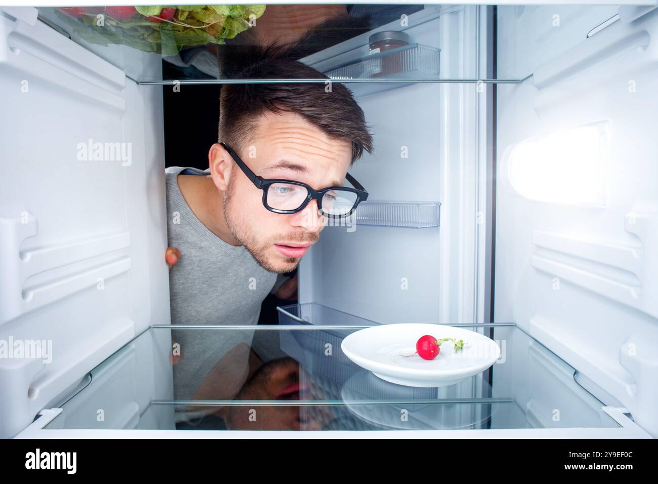 Ein verwirrter Mann, der in einen fast leeren Kühlschrank schaut Stockfoto