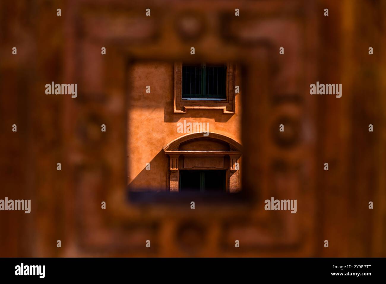 Altes Fenster eines alten Gebäudes aus dem quadratischen Loch einer orangen Wand in Ferrara Stockfoto