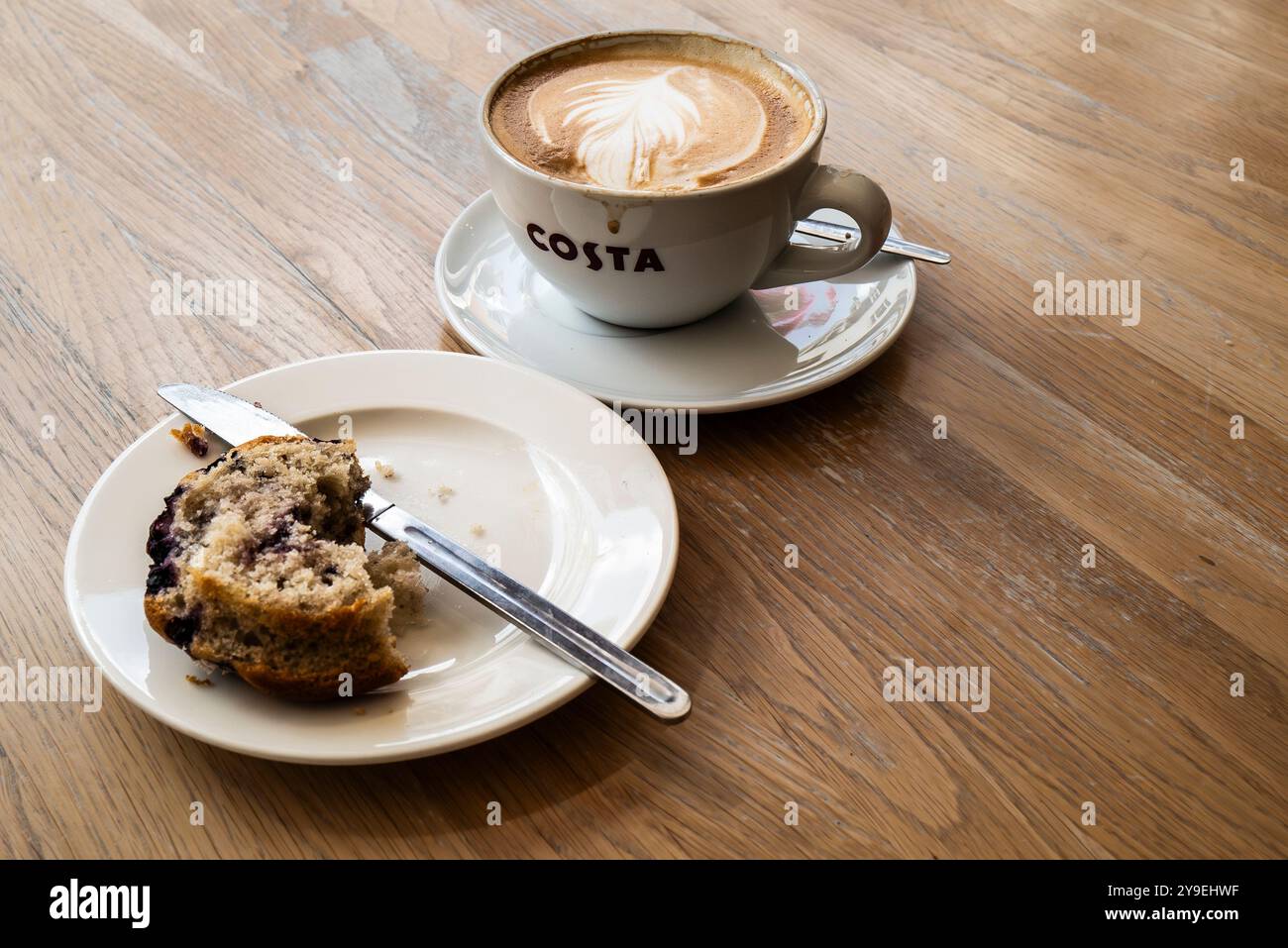 Ein halb gegessen Blaubeermuffin und ein flacher weißer Kaffee auf einem Tisch in einem Costa Coffee Shop im Stadtzentrum von Newquay in Cornwall in Großbritannien. Stockfoto