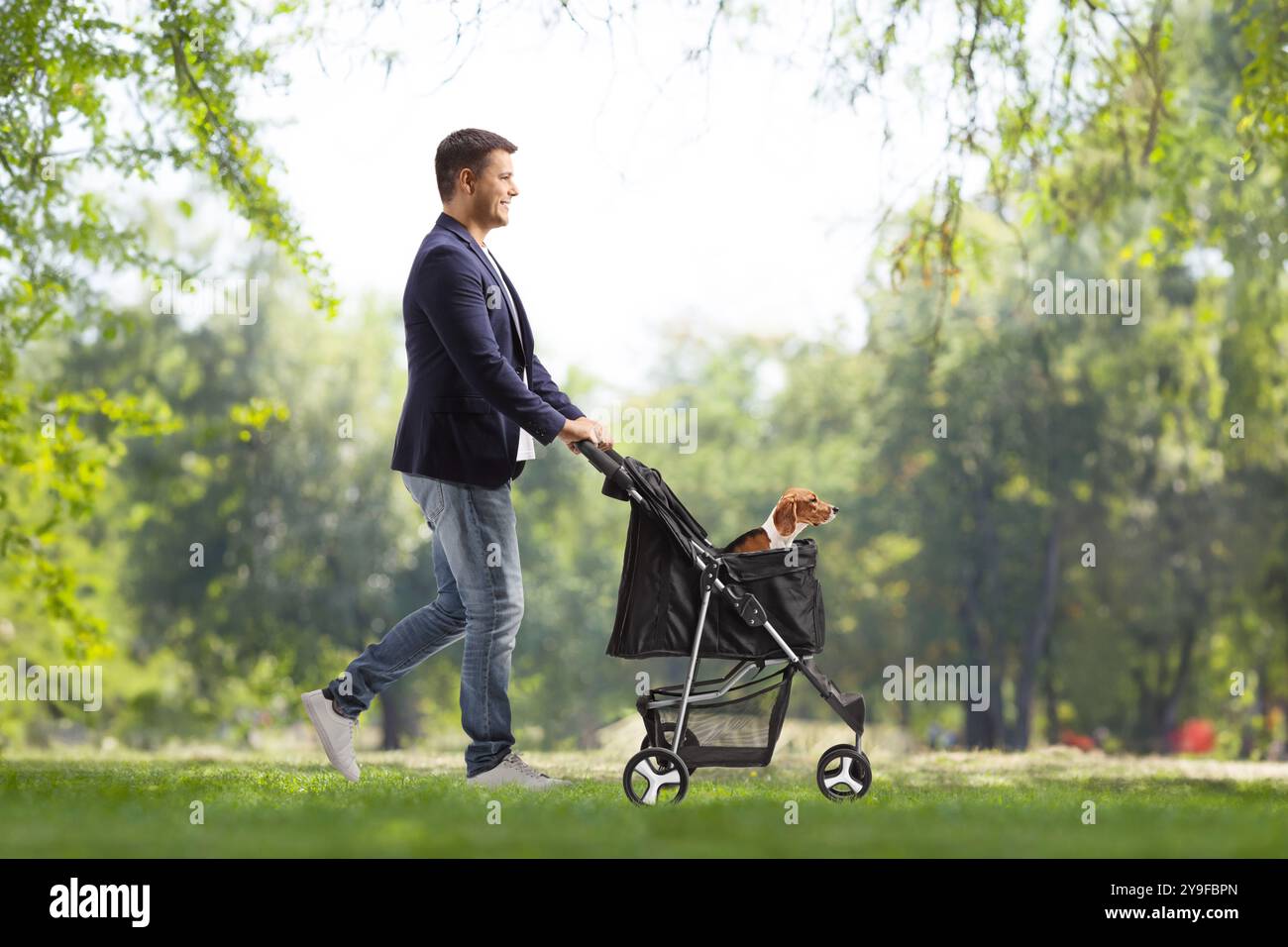 Profilaufnahme eines jungen Mannes, der in einem Park läuft und einen Hundewagen schiebt Stockfoto