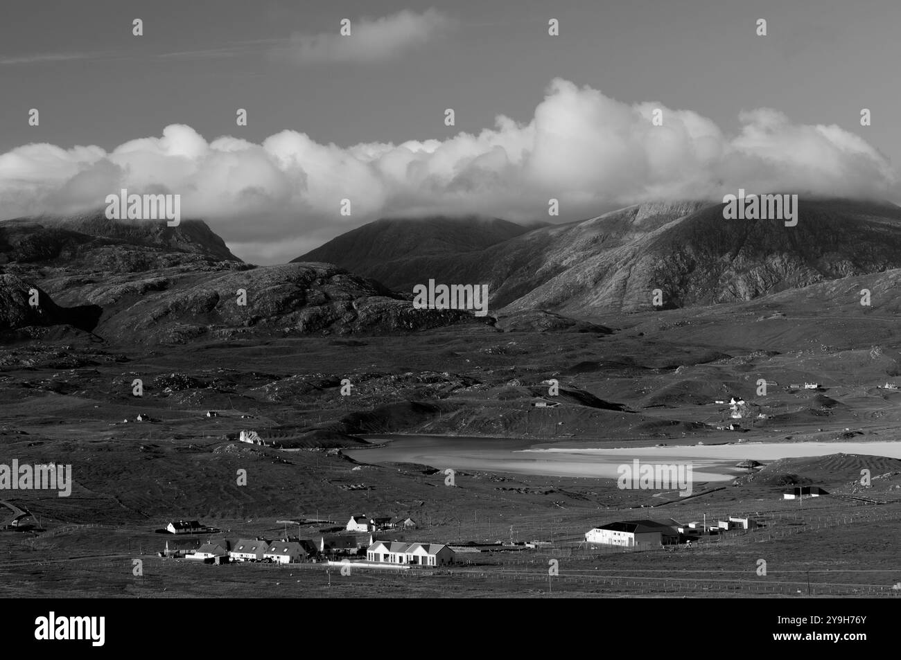 Eine graue Landschaft mit Bergen, die in Wolken gehüllt sind, einer Bucht und einem kleinen Dorf, das die ruhige Schönheit des ländlichen Lebens einfängt. Stockfoto