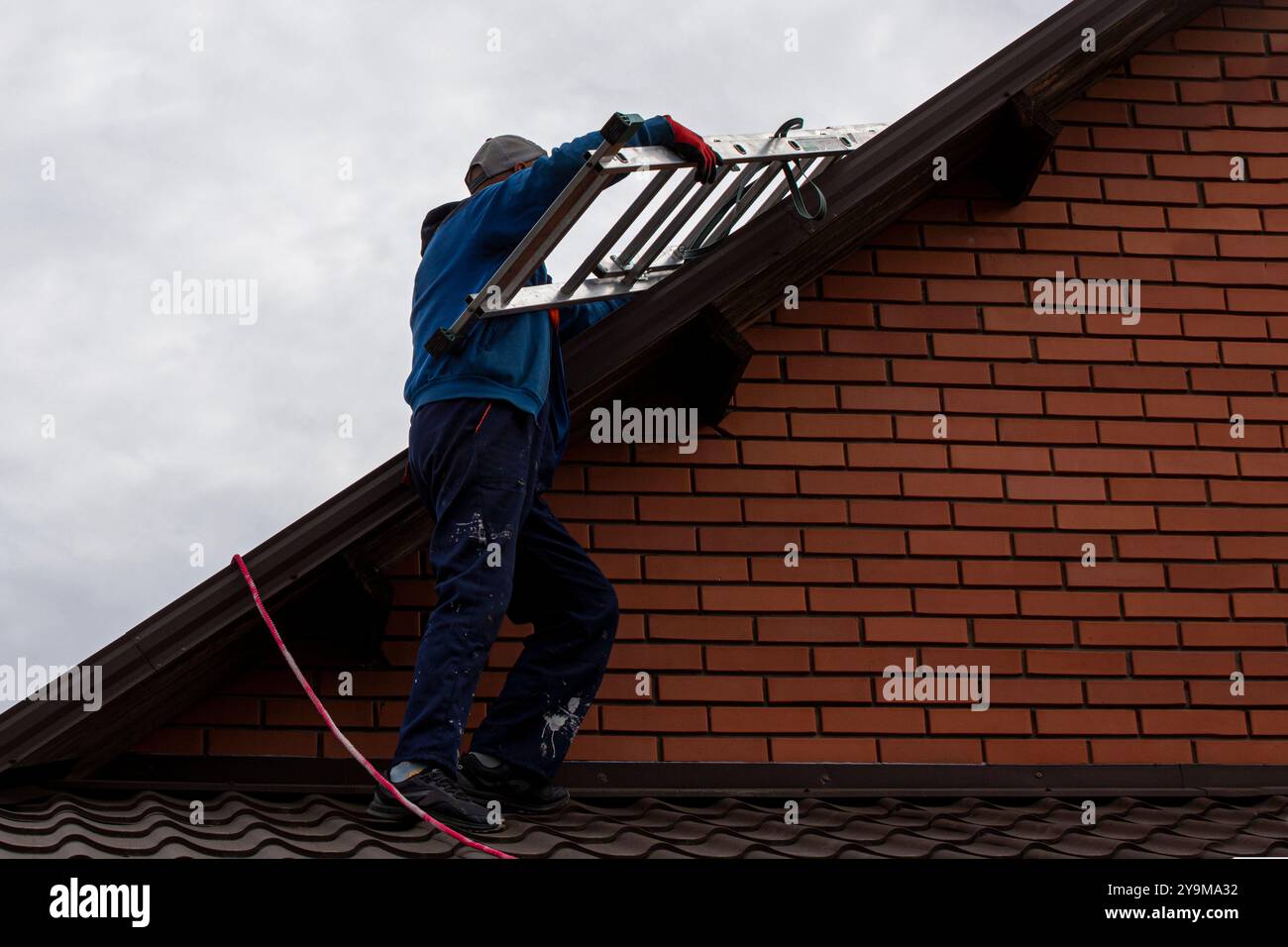 Der Arbeiter hebt eine Leiter auf das Dach, bevor er Solarpaneele installiert. Energieeinsparung der Erde Stockfoto