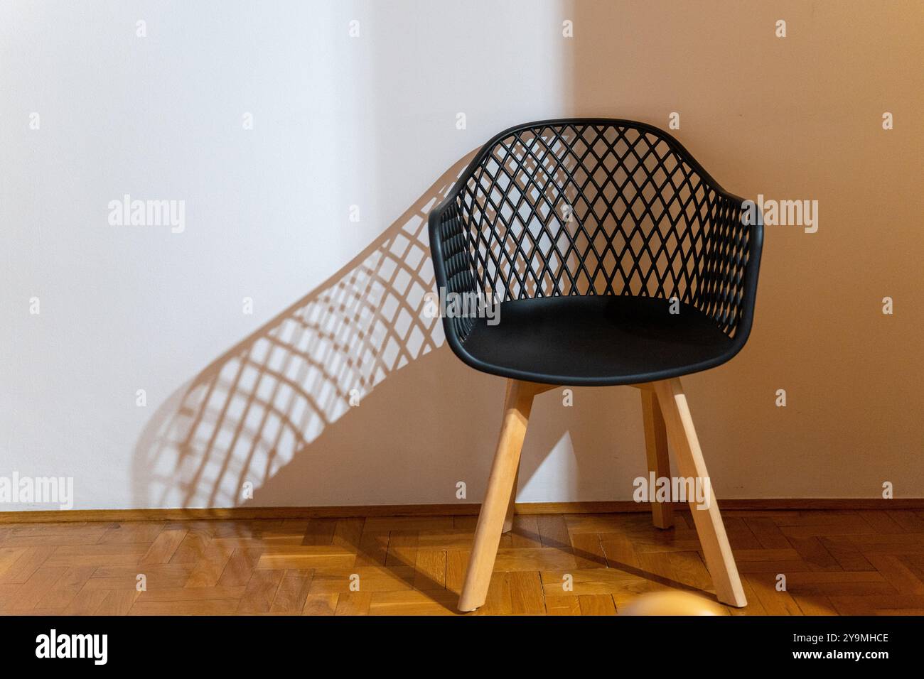 Schwarzer Kunststoffstuhl mit Holzbeinen: Licht, Schatten und Reflexion in einem Raum Stockfoto Schwarzer Kunststoffstuhl mit Holzbeinen: Licht, Schatten und Reflexion in einem Raum Stockfoto