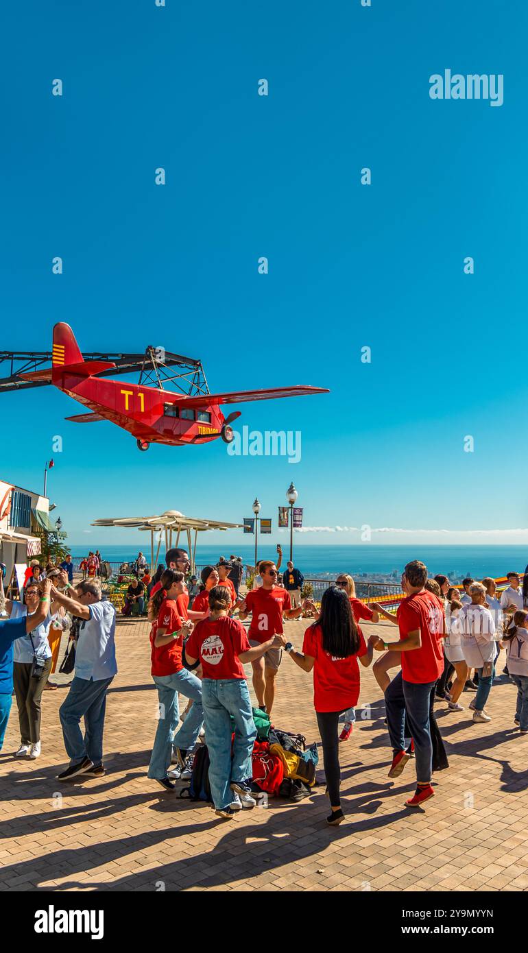 Die Menschen tanzen katalanische Sardanas im Kreis bei einem Outdoor-Event mit der Anziehungskraft eines roten Flugzeugs, das an einem sonnigen Tag mit dem Meer in Th über sie fährt Stockfoto