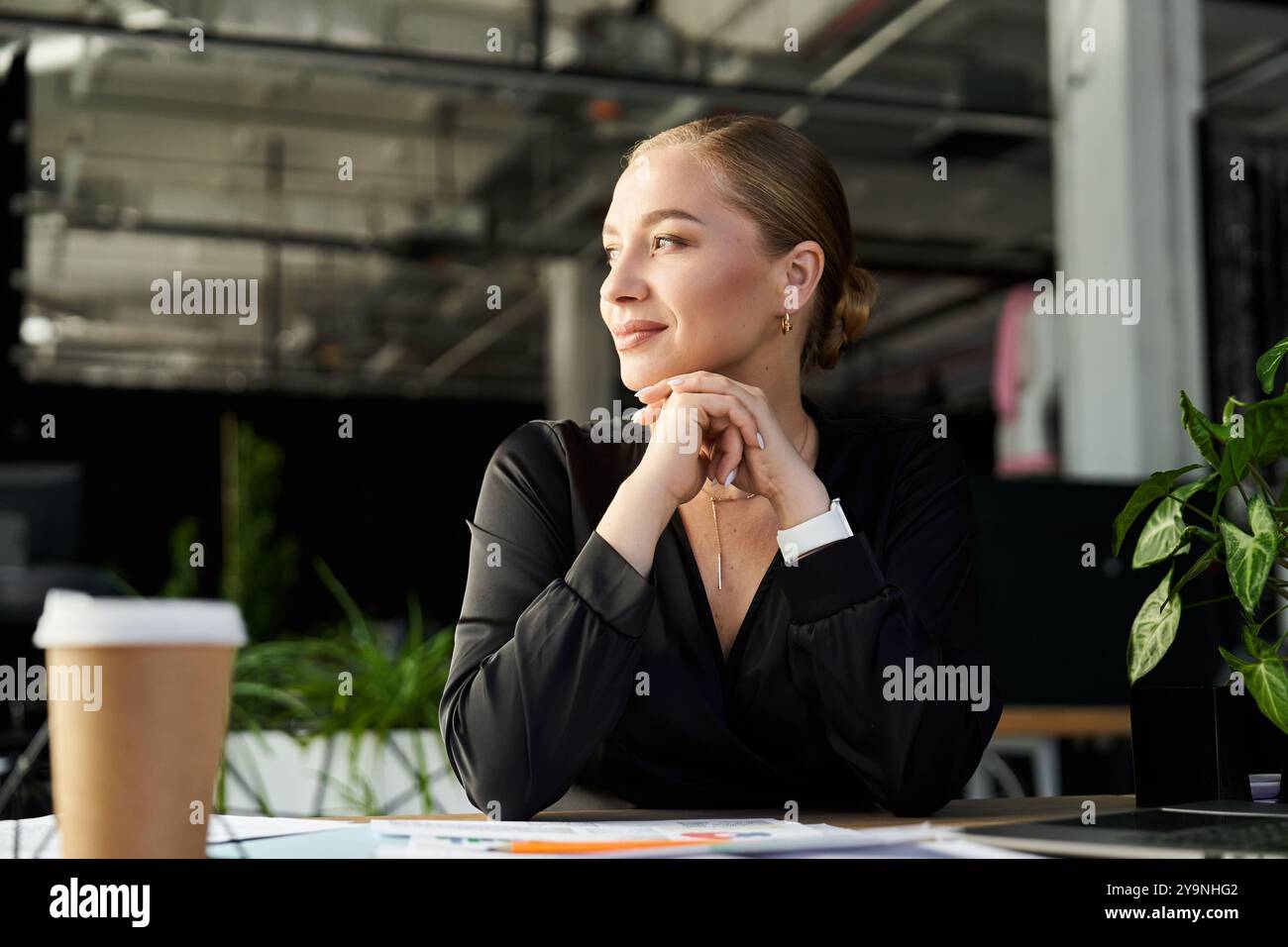 Eine junge, schöne Frau in Übergröße in einem Büro reflektiert sich, während sie an ihrem Schreibtisch arbeitet. Stockfoto