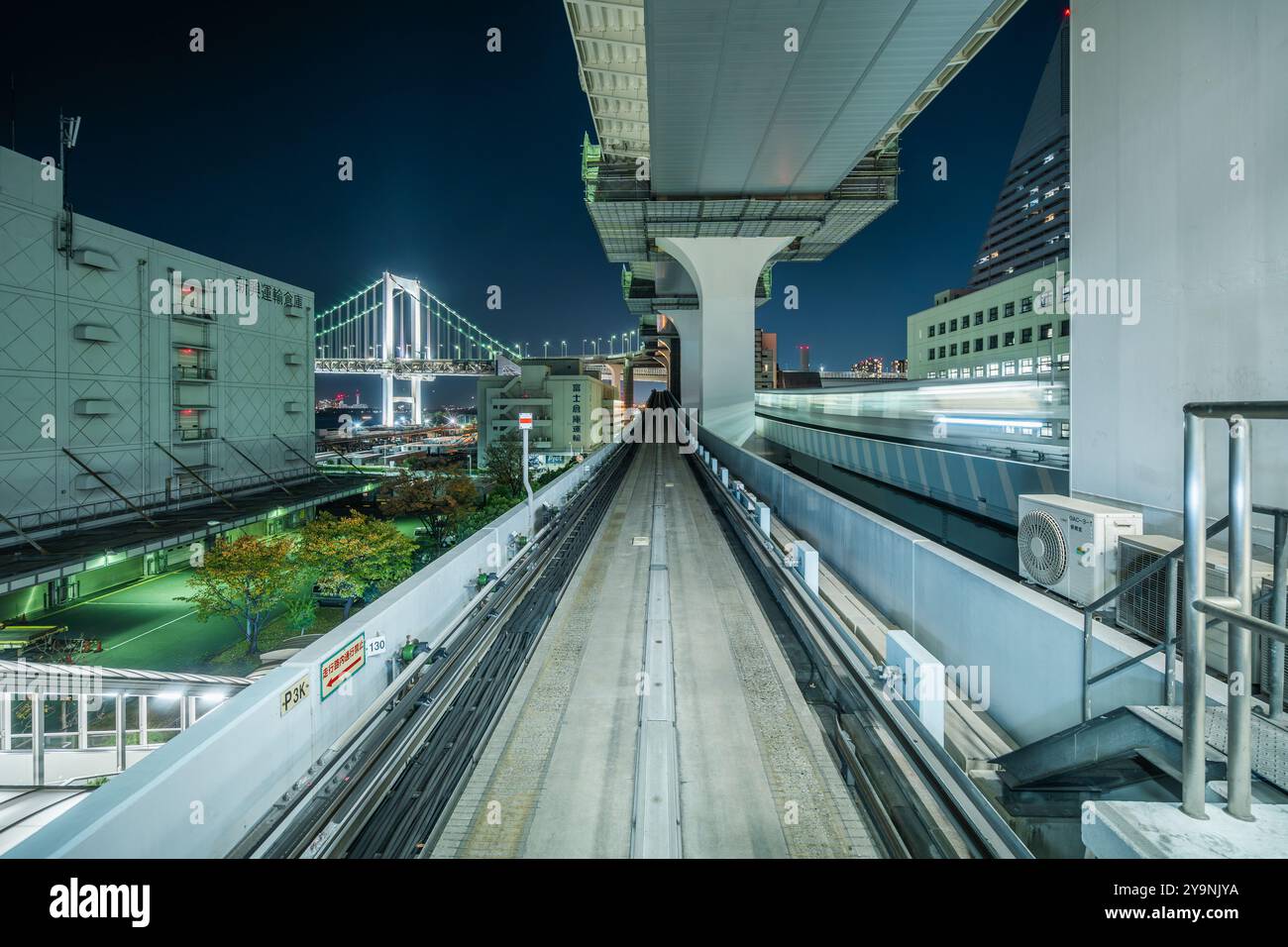 POV-Aufnahme der Yurikamome-Linie bei Nacht mit architektonischem Wahrzeichen der Rainbow Bridge in der Ferne in Tokio, Japan. Stockfoto