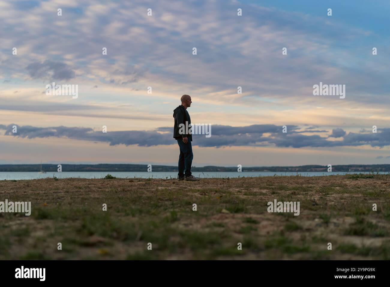 Ein Mann vor dem Hintergrund des Sonnenuntergangs am Ufer eines Sees. Stockfoto