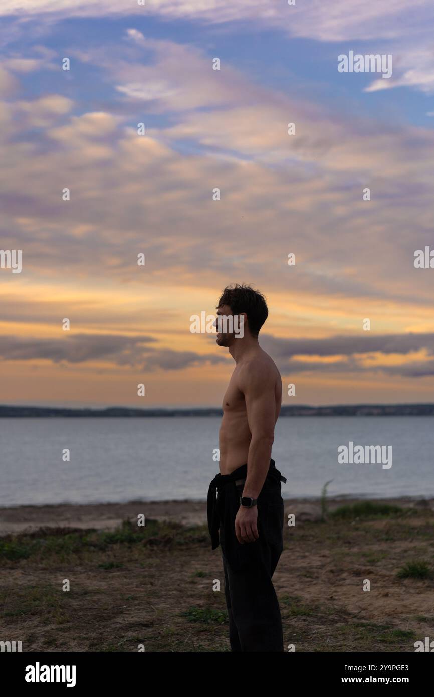 Ein Mann vor dem Hintergrund des Sonnenuntergangs am Ufer eines Sees. Stockfoto