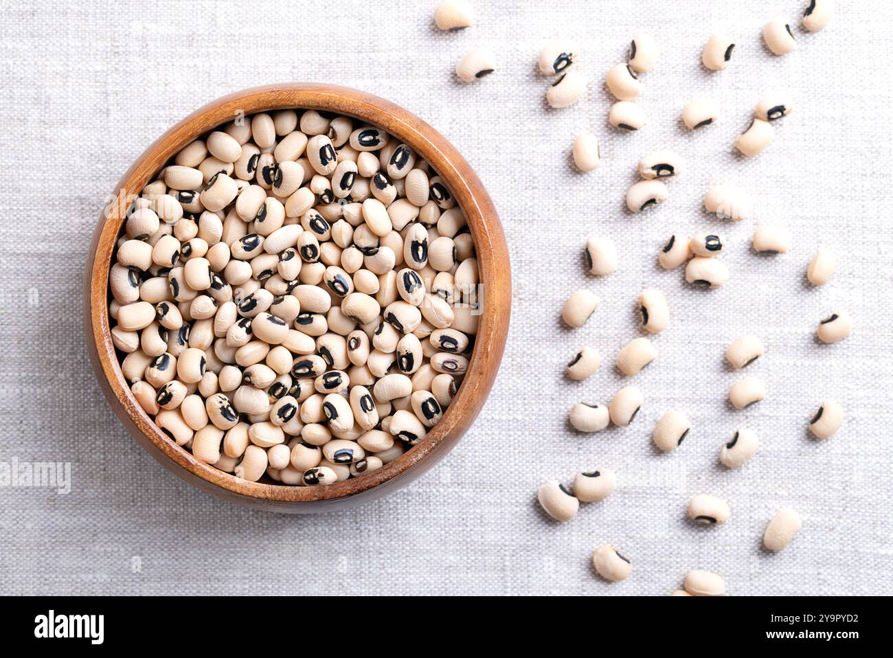 Getrocknete Erbsen mit schwarzen Augen in einer Holzschale über Leinen. Schwarze Bohnen oder kalifornische Schwarzauge, eine Hülse aus hellen, mittelgroßen Bohnen mit schwarzem Fleck. Stockfoto Getrocknete Erbsen mit schwarzen Augen in einer Holzschale über Leinen. Schwarze Bohnen oder kalifornische Schwarzauge, eine Hülse aus hellen, mittelgroßen Bohnen mit schwarzem Fleck. Stockfoto