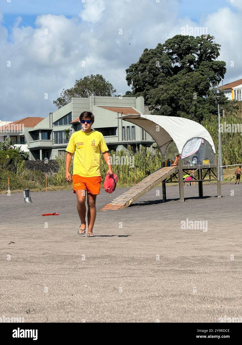 Rettungsschwimmer an einem schwarzen Sandstrand auf der Insel São Miguel, Azoren, Portugal, mit Flossen und Rettungskanne an einem sonnigen Sommertag. - Smartphone-aufgenommenes Stockfoto