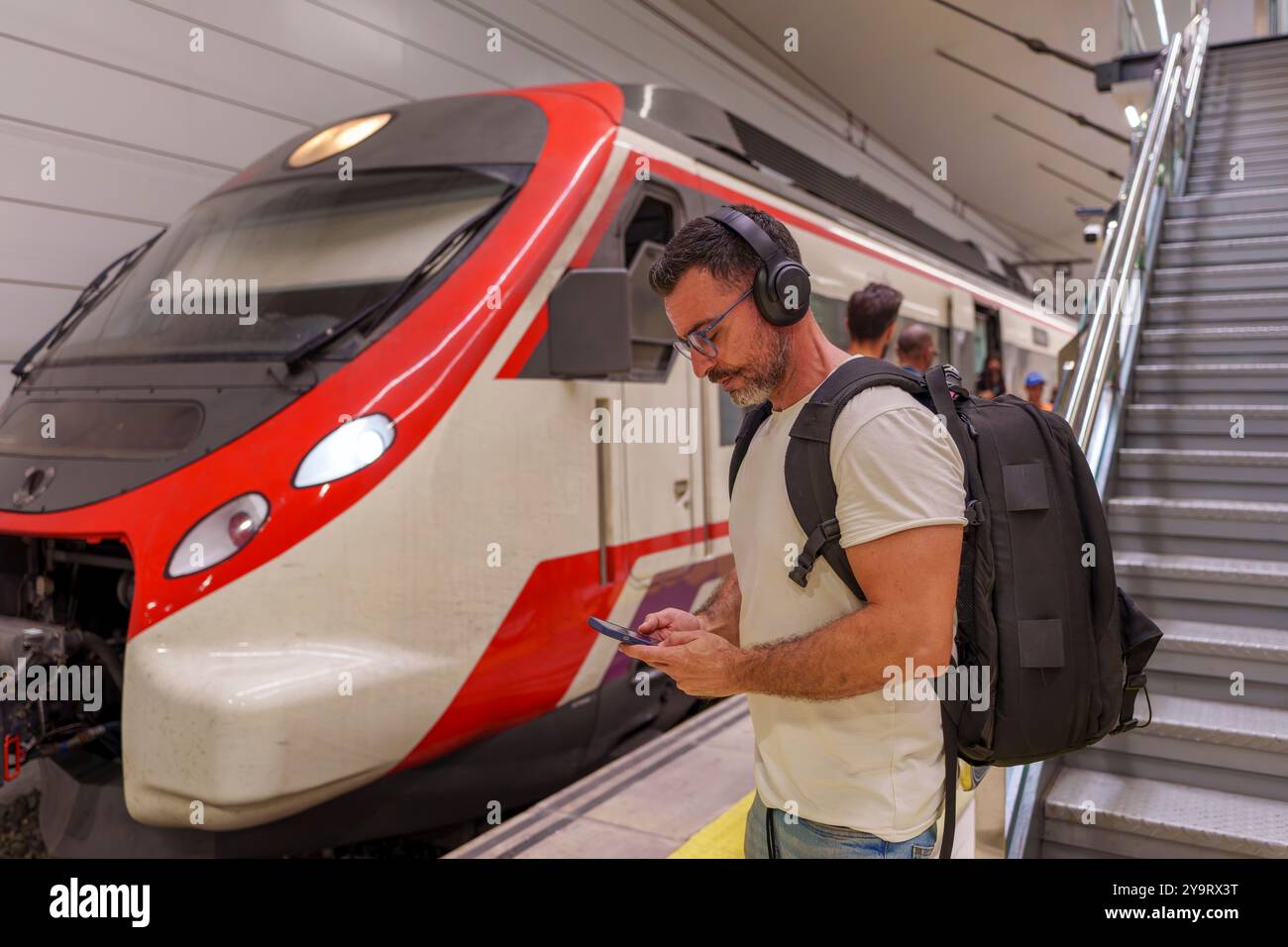 Mann mittleren Alters in Freizeitkleidung mit Smartphone für E-Ticket am Bahnhof Stockfoto