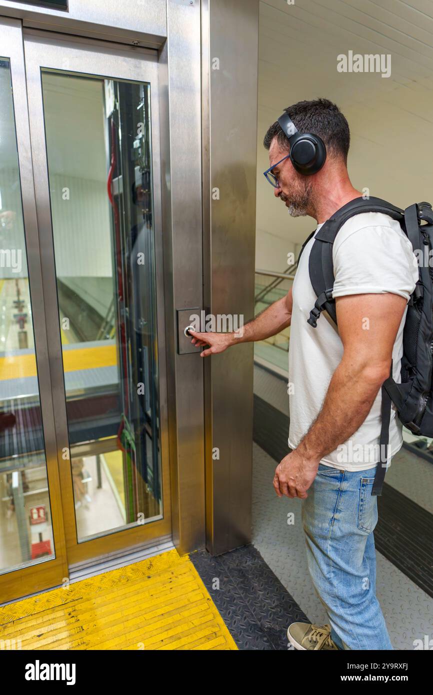 Mann mittleren Alters in lässiger Kleidung mit Rucksack, der den Aufzug am Bahnhof anruft, um Bahnsteige zu erreichen Stockfoto