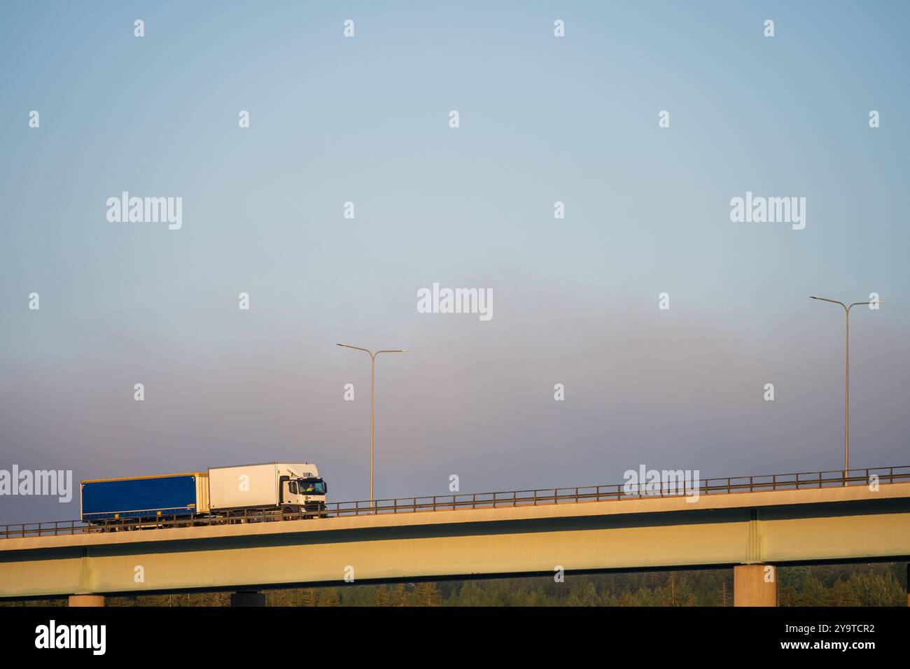 Ein weißer und blauer großer Lkw fährt über eine Autobahnbrücke gegen den Morgenhimmel Stockfoto