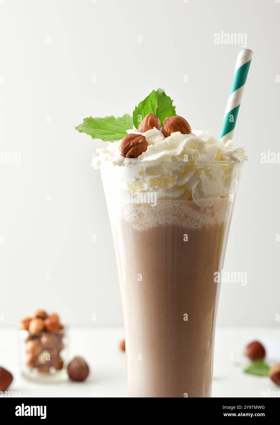 Detail des Milchshakes mit Haselnüssen und Sahne dekoriert mit Nüssen und Blättern in einem Glas mit Strohhalm und weißem Hintergrund isoliert. Vorderansicht. Stockfoto