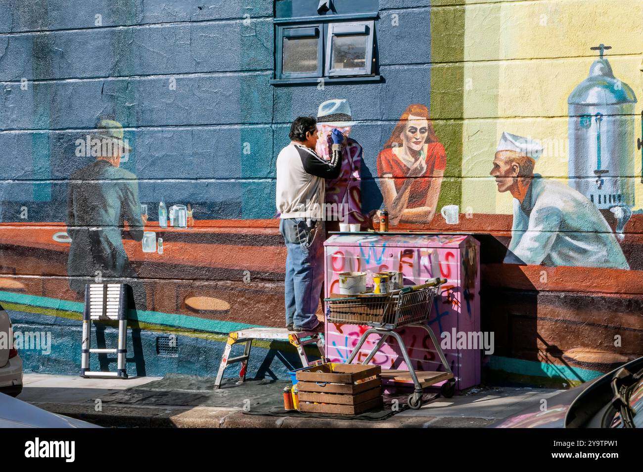 Straßenkünstler arbeitet an einem Wandbild in Camden Town London. Das Wandbild ist eine Version der Nighthawks von Edward Hopper. Stockfoto