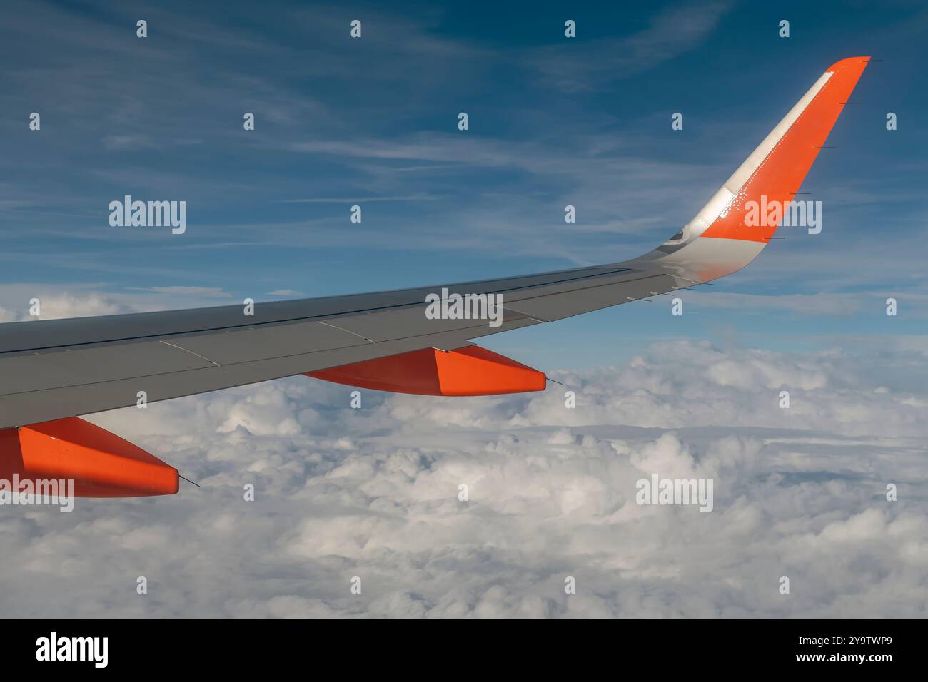 Der Flügel eines Flugzeugs gegen den blauen Himmel und eine Schicht weißer Wolken darunter Stockfoto