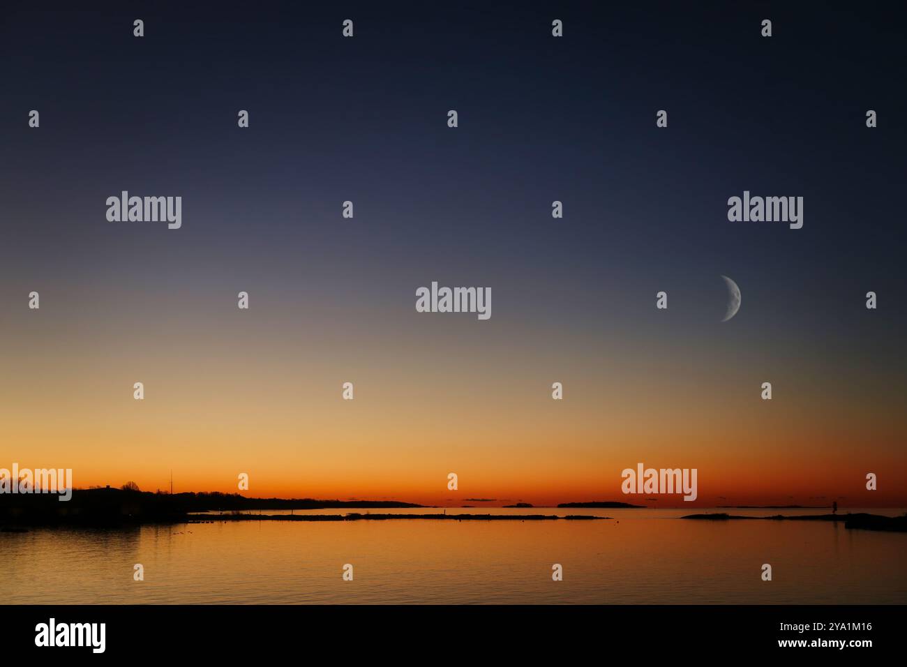 Glühender Morgenhimmel mit sichelndem Mond über dem Meer vor Tagesanbruch in Finnland an einem ruhigen Novembermorgen. Stockfoto