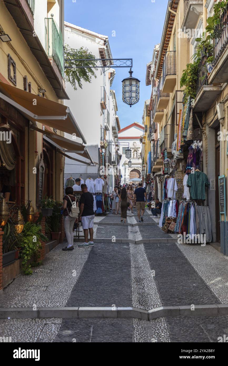 Lebhafte Einkaufsstraße mit Menschen zwischen historischen Gebäuden unter blauem Himmel, Granada Stockfoto