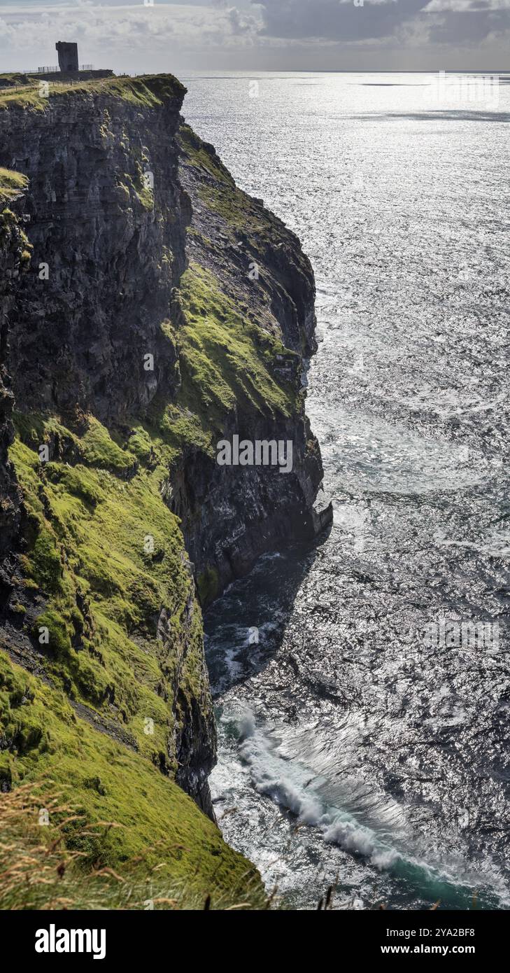 Zerklüftete Klippen, die von Sonnenlicht beleuchtet werden, erheben sich über dem glitzernden Meer, den Cliffs of Moher Stockfoto