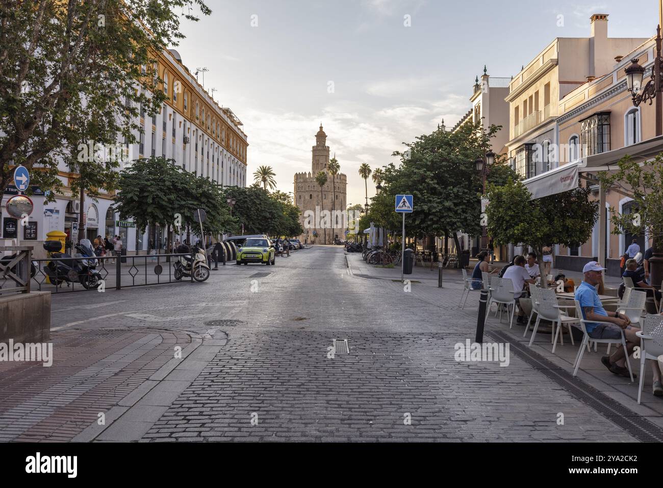 Straßenszene bei Sonnenuntergang mit Cafés, gesäumt von Bäumen und Gebäuden, Sevilla Stockfoto