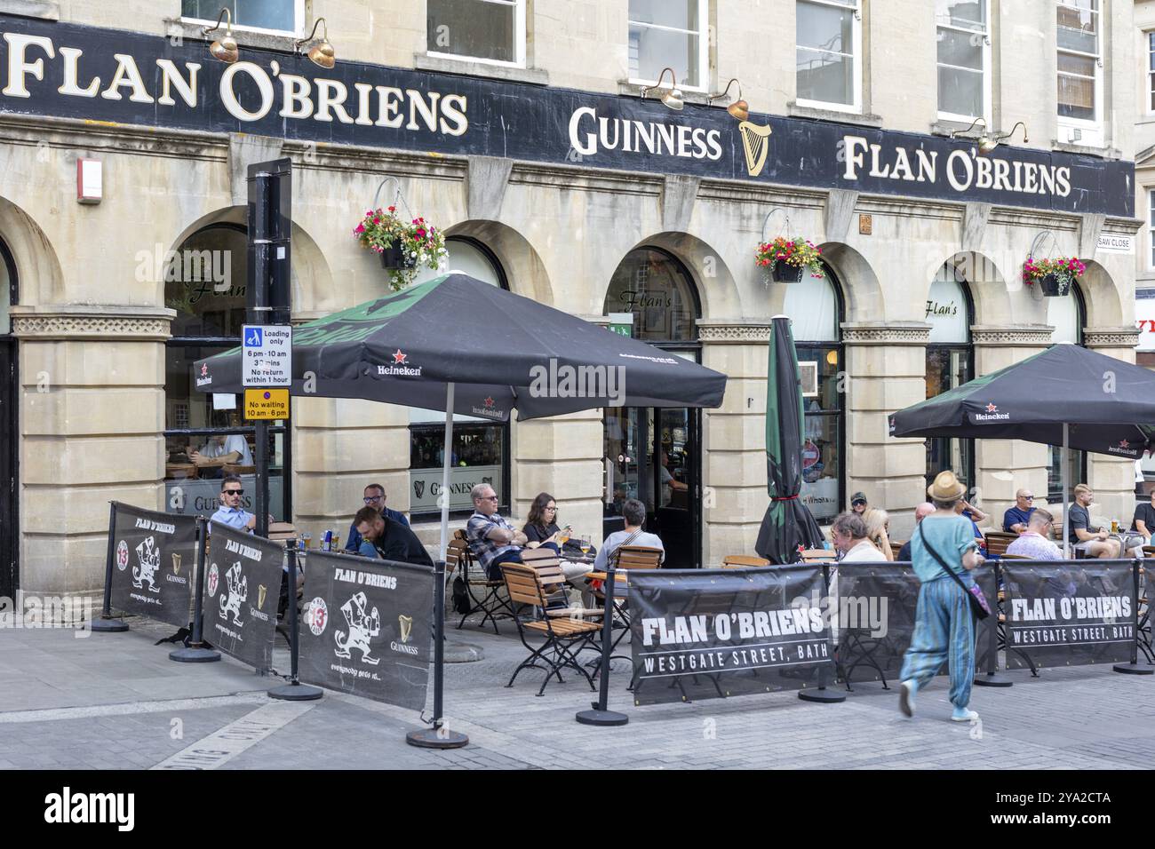 Gäste des Cafés sitzen unter Sonnenschirmen vor einem traditionellen Pub in einer geschäftigen Straße, Bath Stockfoto