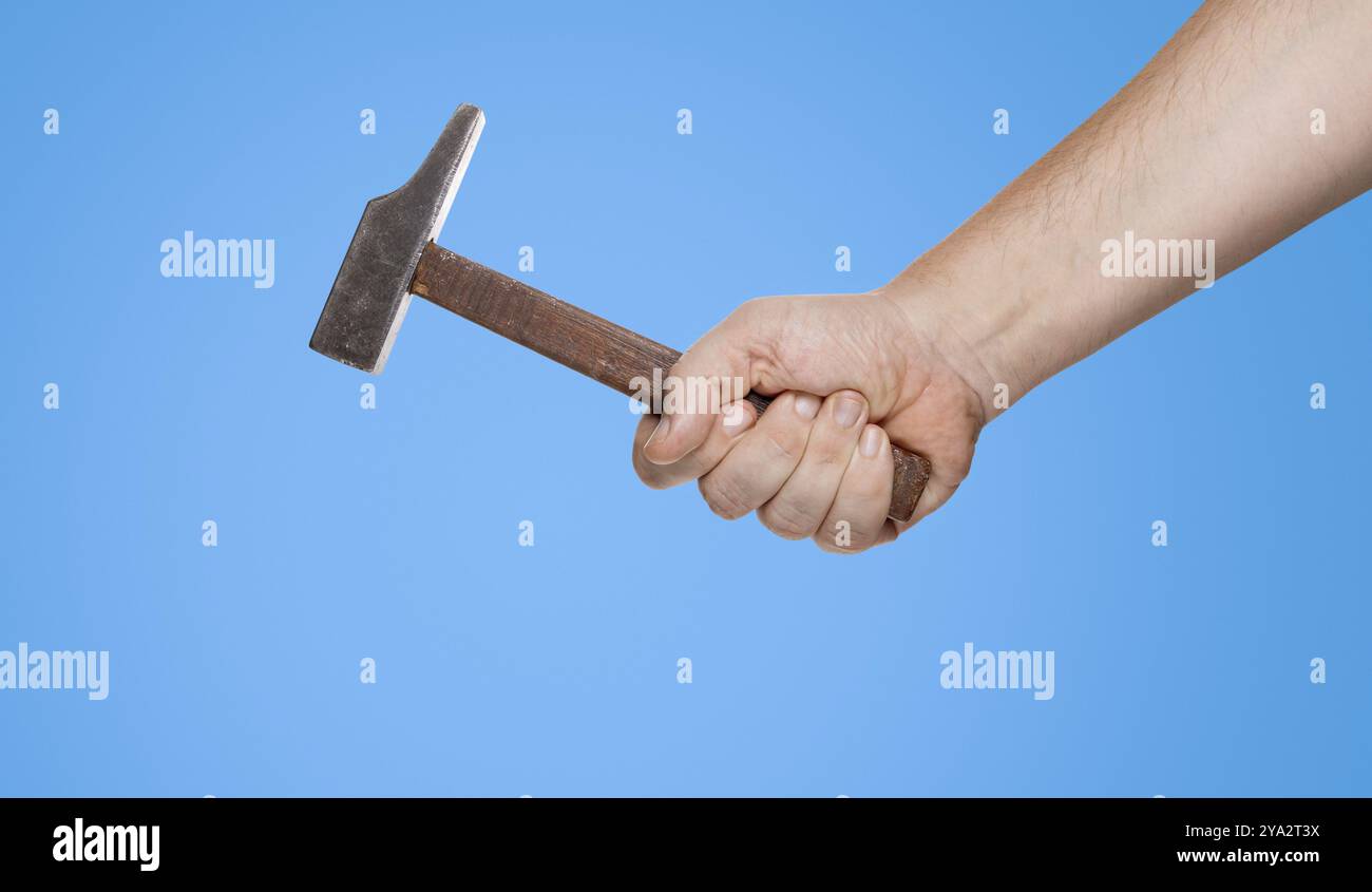 Ein Mann hält einen Hammer in der Hand vor einem blauen Hintergrund Stockfoto