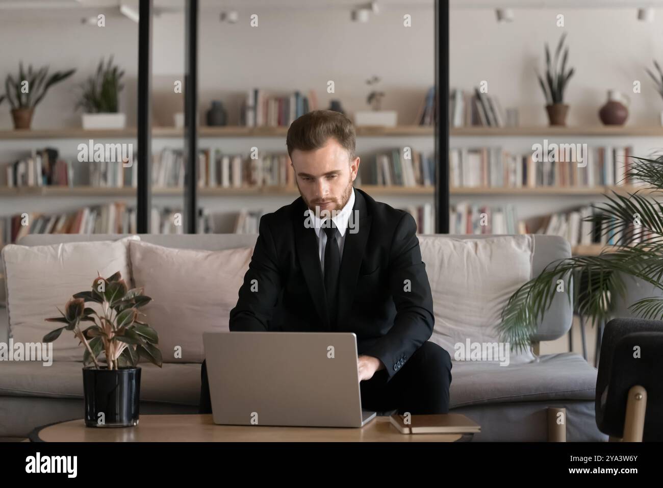 Ernsthafter junger Geschäftsmann in Anzug und Krawatte, der am Laptop arbeitet Stockfoto