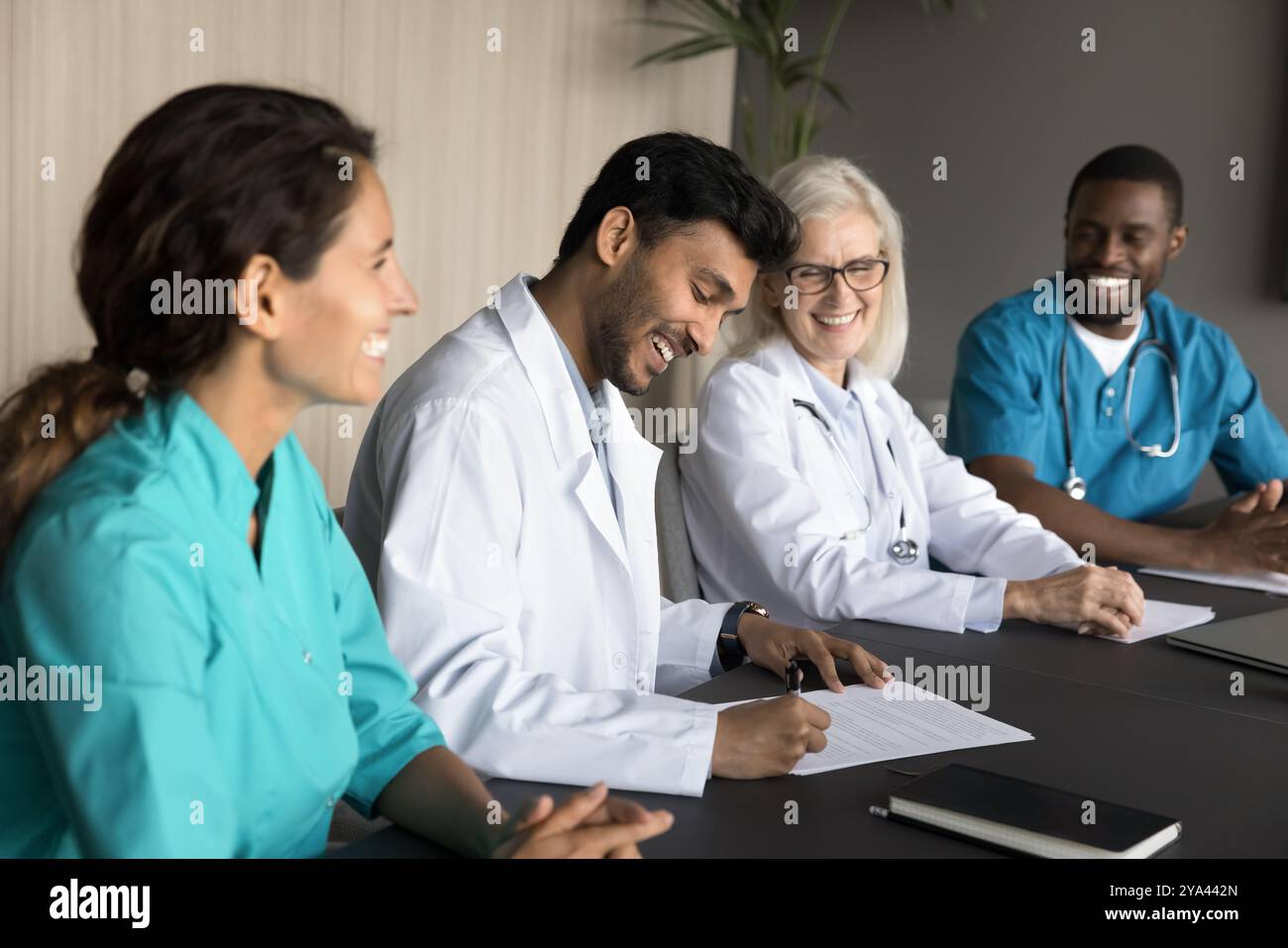 Glücklicher junger männlicher Arzt unterschreibt Arbeitsvertrag mit dem modernen Krankenhaus Stockfoto