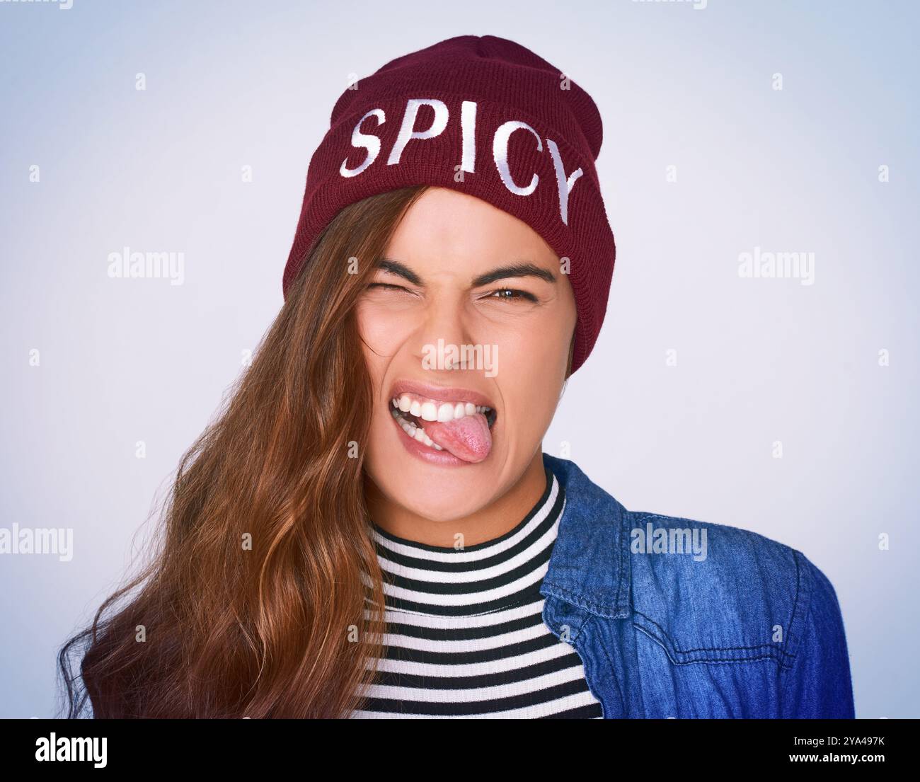 Porträt, Frau und Rebelle mit albernem Ausdruck im Studio für wilde Attitüde, flippige Mode und scharfe Beanie. Blöd, Mädchen und stecke die Zunge aus Stockfoto