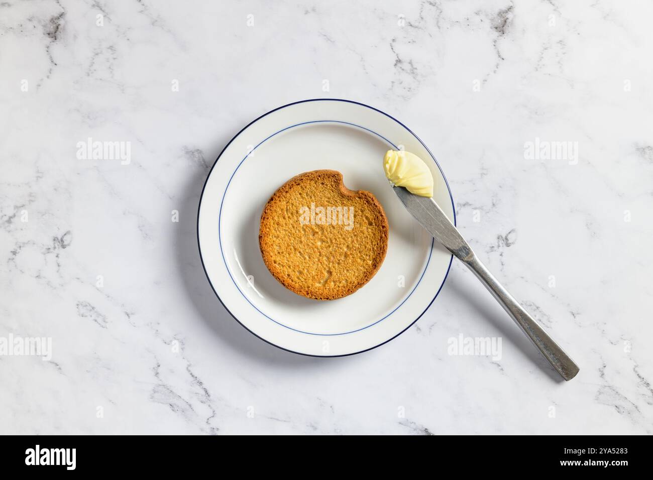 Blick von oben auf eine traditionelle niederländische russe und ein Küchenmesser mit cremiger Butter auf einer weißen Keramikplatte vor einem Marmorhintergrund. Stockfoto