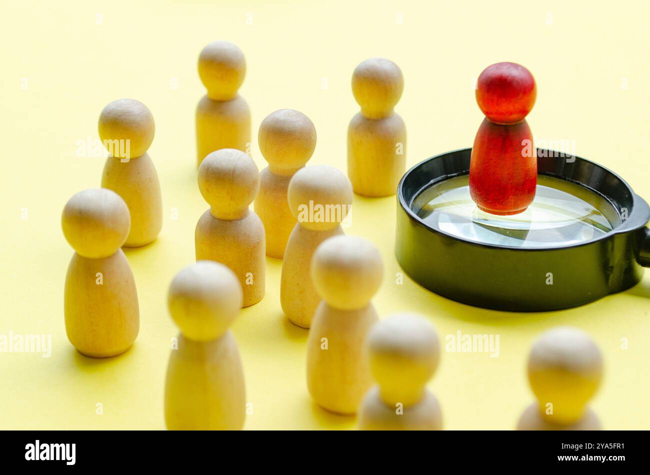 Eine rote Holzfigur, die auf einer Lupe steht und den Rest der anderen Figur führt. Führungskonzept Stockfoto