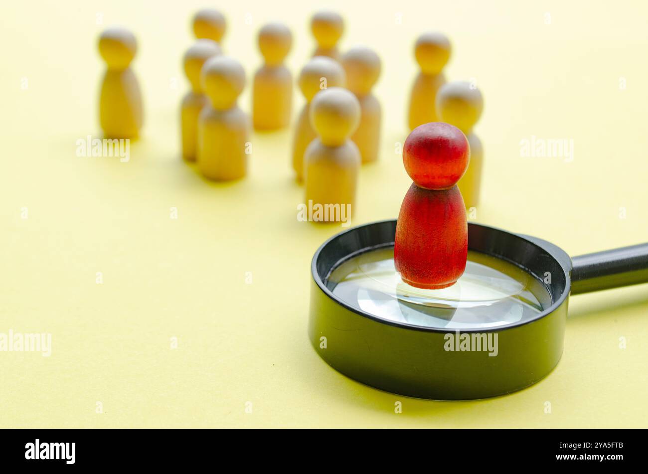 Eine rote Holzfigur, die auf einer Lupe steht und den Rest der anderen Figur führt. Führungskonzept. Stockfoto
