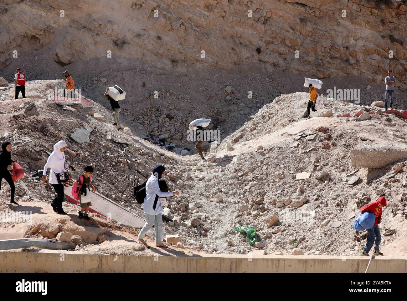 Grenzübergang Masnaa, Libanon. Oktober 2024. Dieses Foto zeigt Vertriebene aus dem Libanon, die ein Loch auf der Straße überqueren, das durch einen israelischen Luftangriff in der Nähe des Grenzübergangs Masnaa im Libanon am 11. Oktober 2024 verursacht wurde. Vor etwa einer Woche traf der israelische Luftangriff die Grenze zwischen Syrien und Libanon, bekannt als Jdeidat-Jabous-Überquerung in Syrien und Masnaa-Überquerung im Libanon, eine wichtige Transitroute, die von Zehntausenden libanesischen Flüchtlingen und syrischen Bürgern genutzt wird, die vor dem israelischen Angriff im Libanon fliehen. Quelle: Bilal Jawich/Xinhua/Alamy Live News Stockfoto