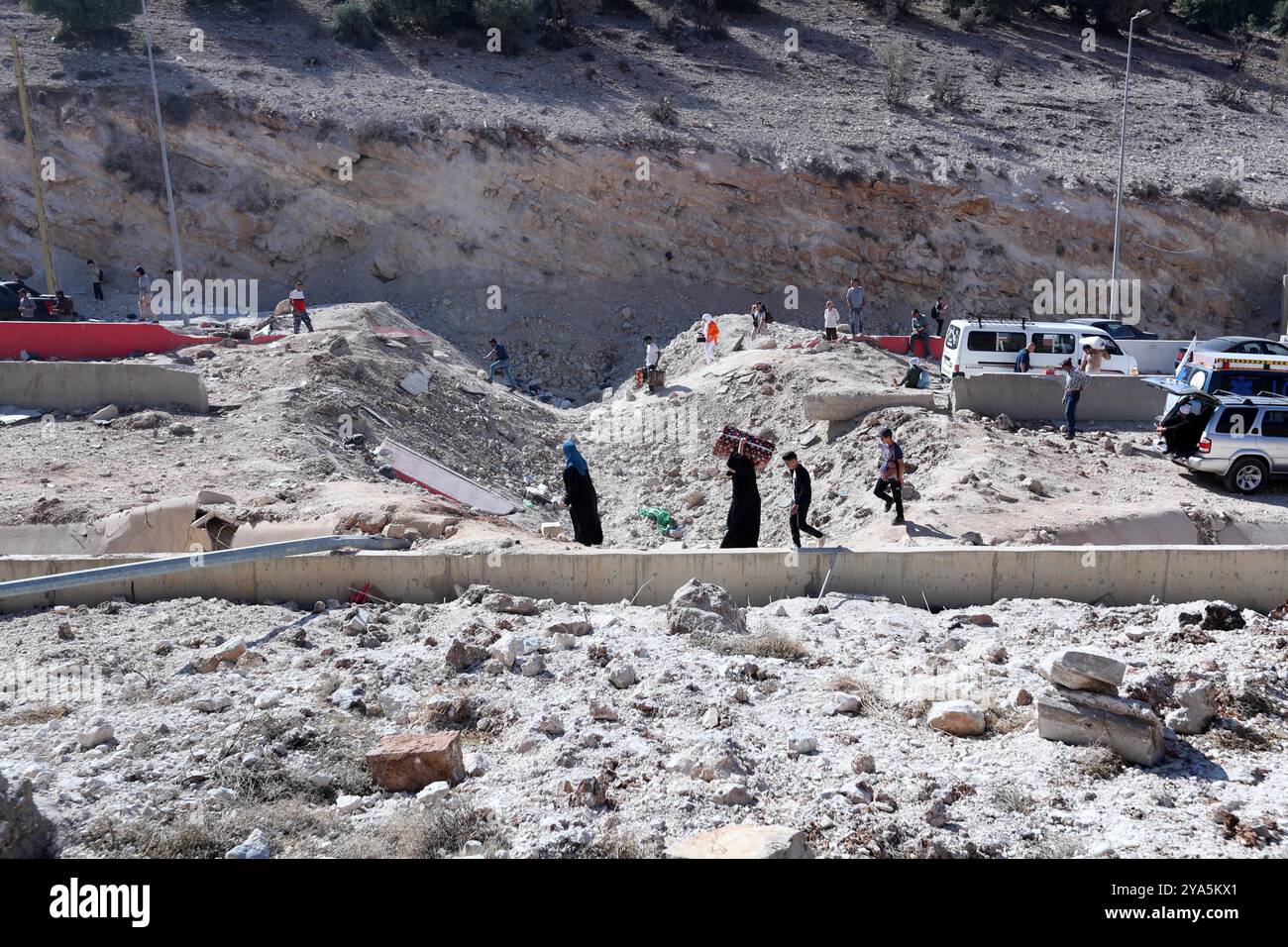 Grenzübergang Masnaa, Libanon. Oktober 2024. Dieses Foto zeigt Vertriebene aus dem Libanon, die ein Loch auf der Straße überqueren, das durch einen israelischen Luftangriff in der Nähe des Grenzübergangs Masnaa im Libanon am 11. Oktober 2024 verursacht wurde. Vor etwa einer Woche traf der israelische Luftangriff die Grenze zwischen Syrien und Libanon, bekannt als Jdeidat-Jabous-Überquerung in Syrien und Masnaa-Überquerung im Libanon, eine wichtige Transitroute, die von Zehntausenden libanesischen Flüchtlingen und syrischen Bürgern genutzt wird, die vor dem israelischen Angriff im Libanon fliehen. Quelle: Bilal Jawich/Xinhua/Alamy Live News Stockfoto