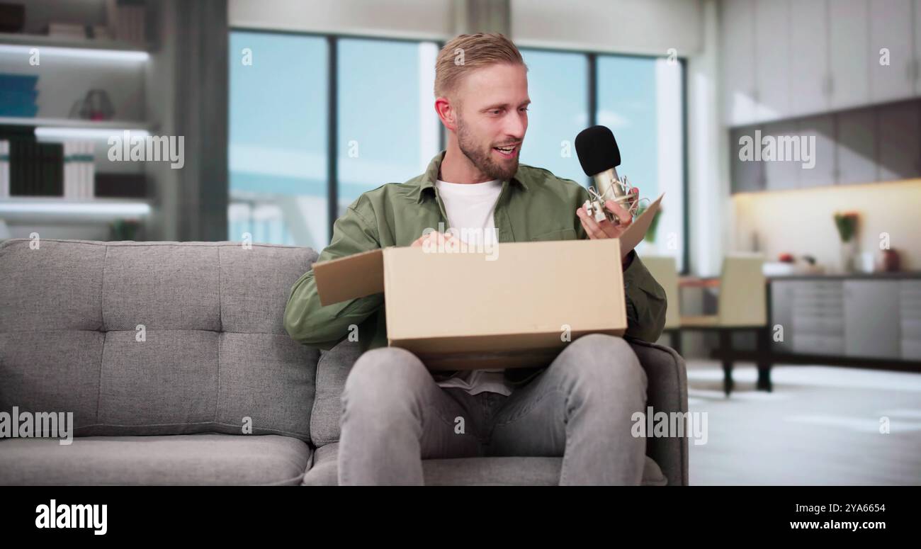 Lächelnden jungen Mann sitzt auf einem Sofa Auspacken empfangene Paket Stockfoto