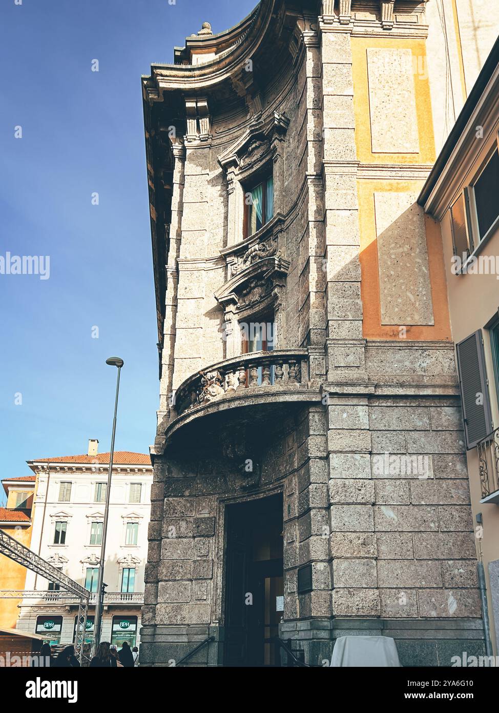 Ein historisches Steingebäude in Monza, Italien, mit kunstvollen architektonischen Details und einem geschwungenen Balkon. Die Sonne wirft Schatten. Stockfoto