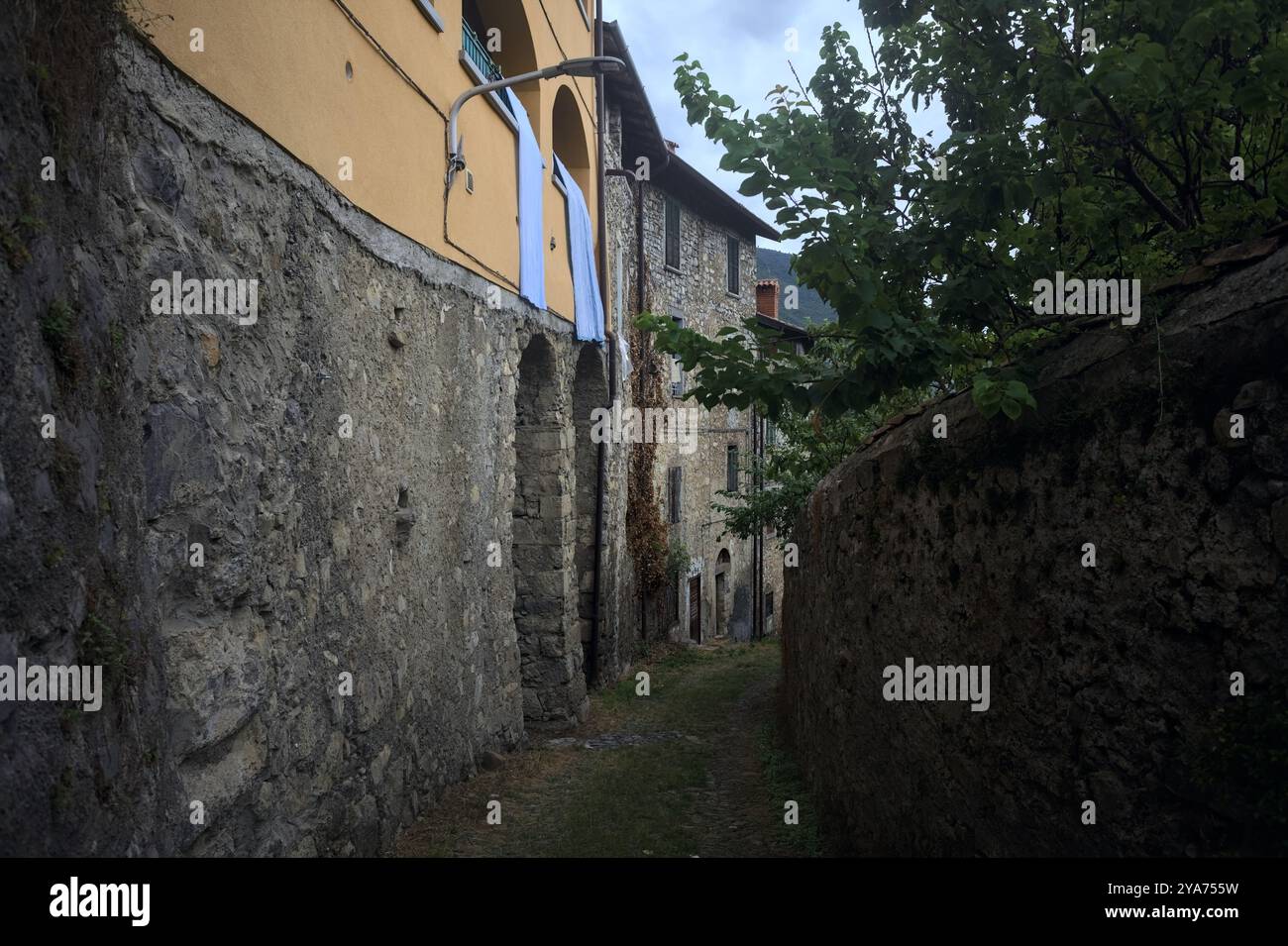 Schlampiger Kopfsteinpflasterweg zwischen einer Steinmauer und einem Steingebäude in den Bergen Stockfoto
