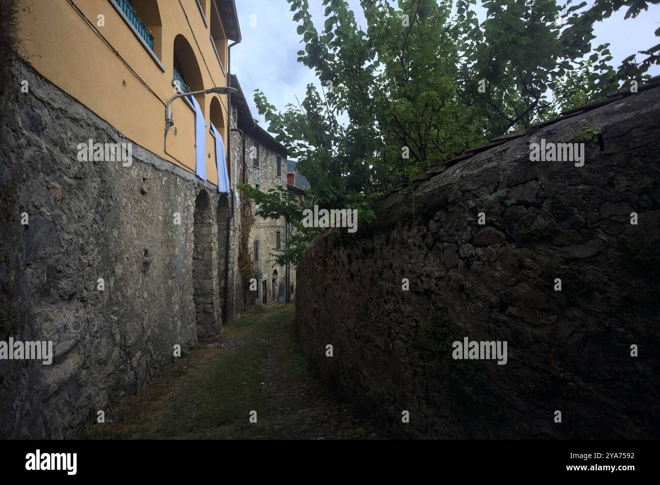 Schlampiger Kopfsteinpflasterweg zwischen einer Steinmauer und einem Steingebäude in den Bergen Stockfoto