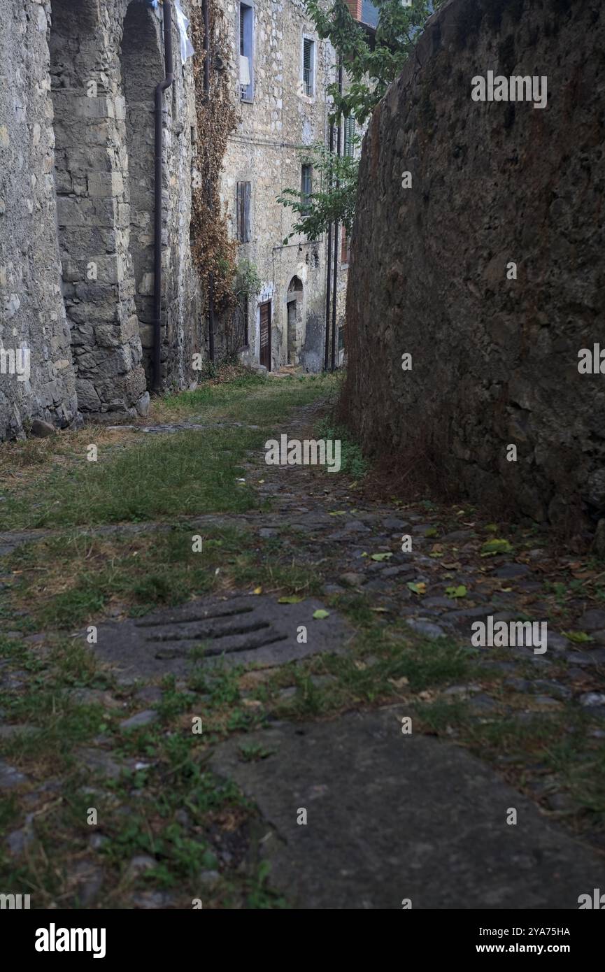 Schlampiger Kopfsteinpflasterweg zwischen einer Steinmauer und einem Steingebäude in den Bergen Stockfoto
