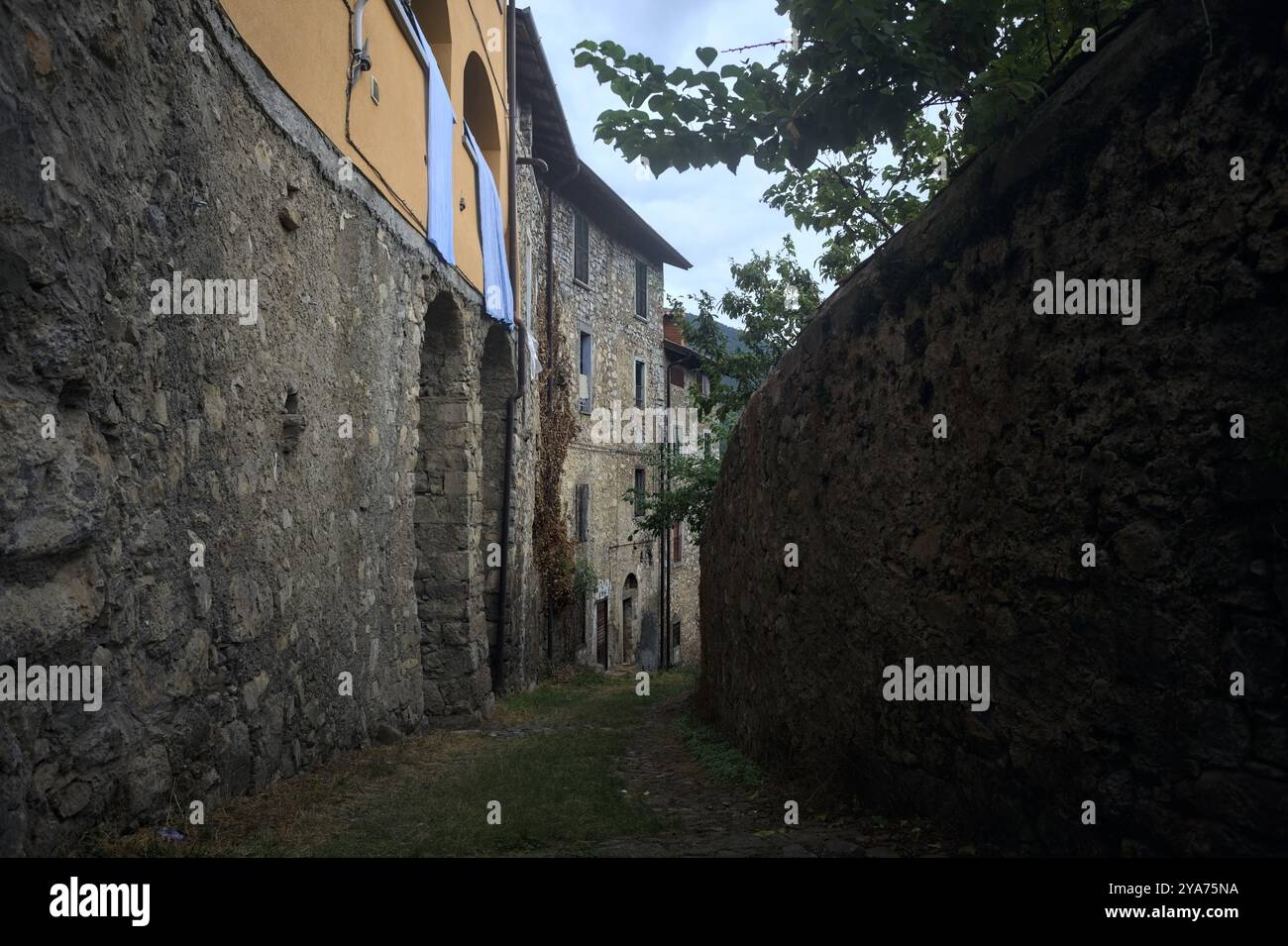 Schlampiger Kopfsteinpflasterweg zwischen einer Steinmauer und einem Steingebäude in den Bergen Stockfoto