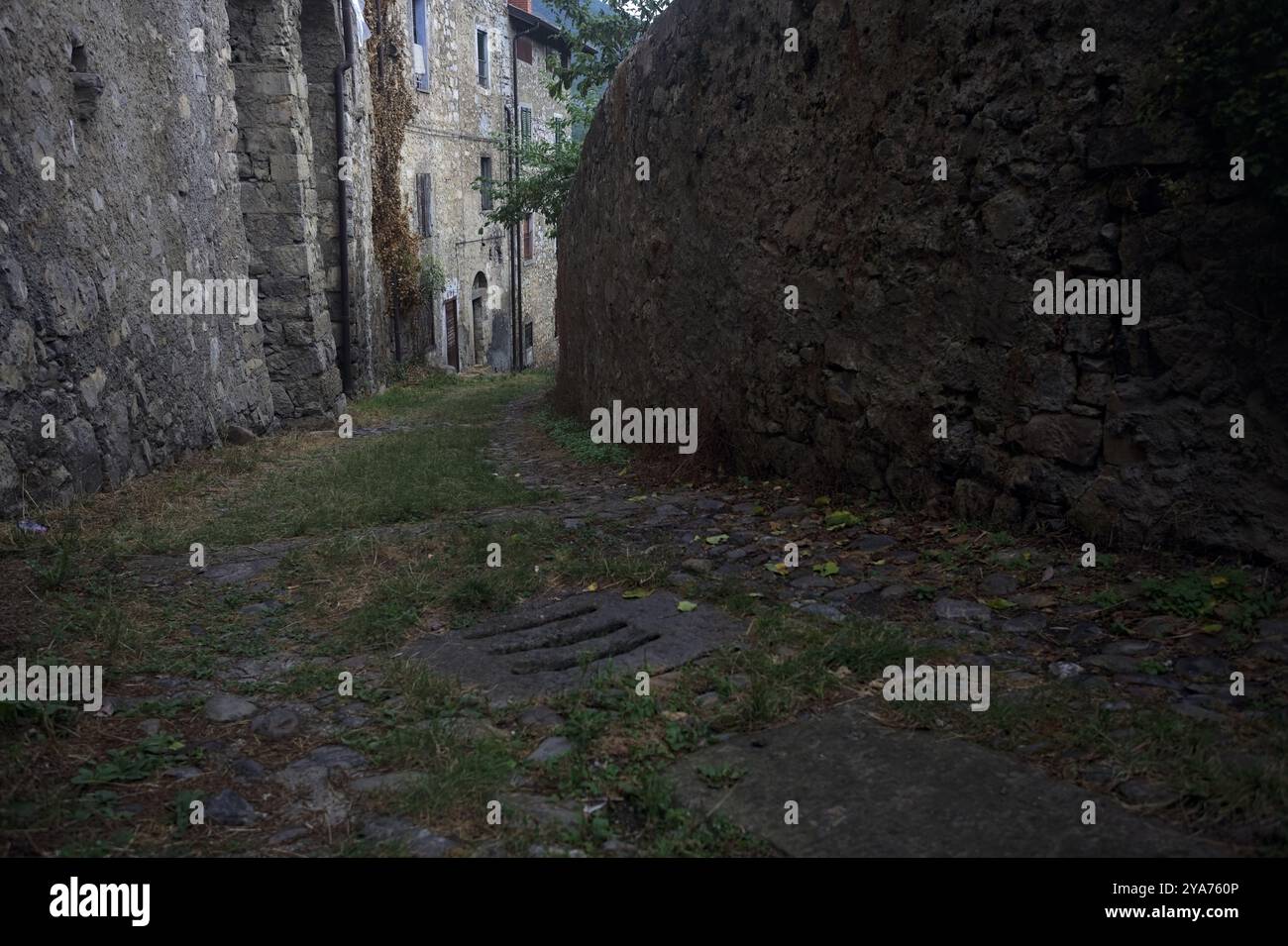 Schlampiger Kopfsteinpflasterweg zwischen einer Steinmauer und einem Steingebäude in den Bergen Stockfoto