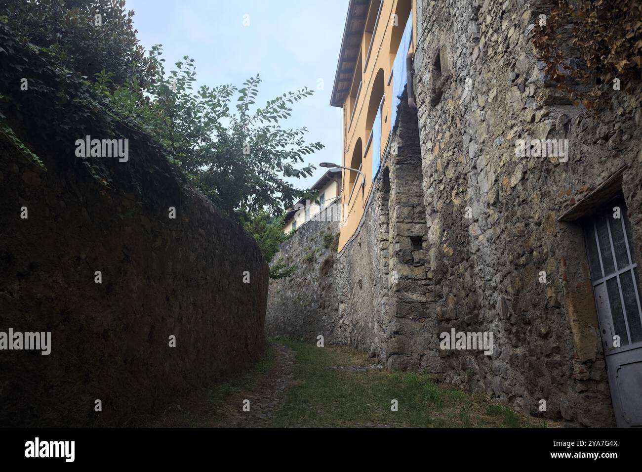 Schlampiger Kopfsteinpflasterweg zwischen einer Steinmauer und einem Steingebäude in den Bergen Stockfoto