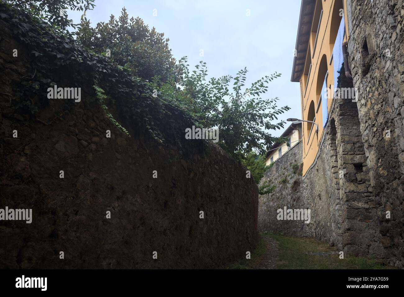Schlampiger Kopfsteinpflasterweg zwischen einer Steinmauer und einem Steingebäude in den Bergen Stockfoto