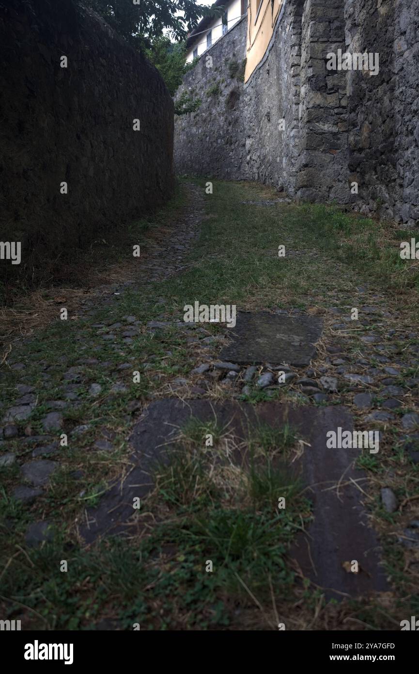 Schlampiger Kopfsteinpflasterweg zwischen einer Steinmauer und einem Steingebäude in den Bergen Stockfoto