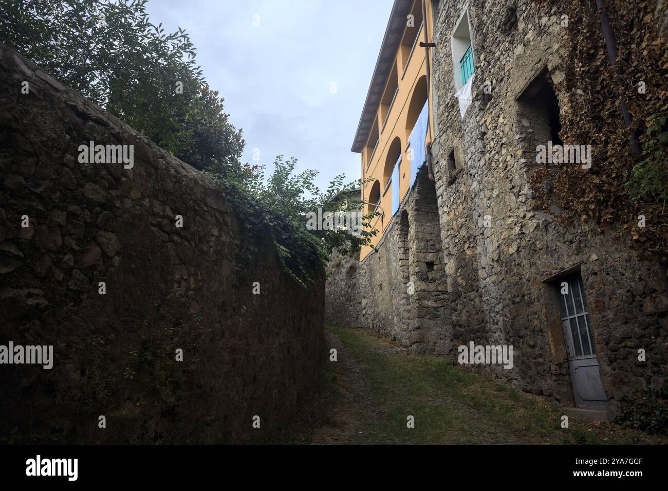 Schlampiger Kopfsteinpflasterweg zwischen einer Steinmauer und einem Steingebäude in den Bergen Stockfoto