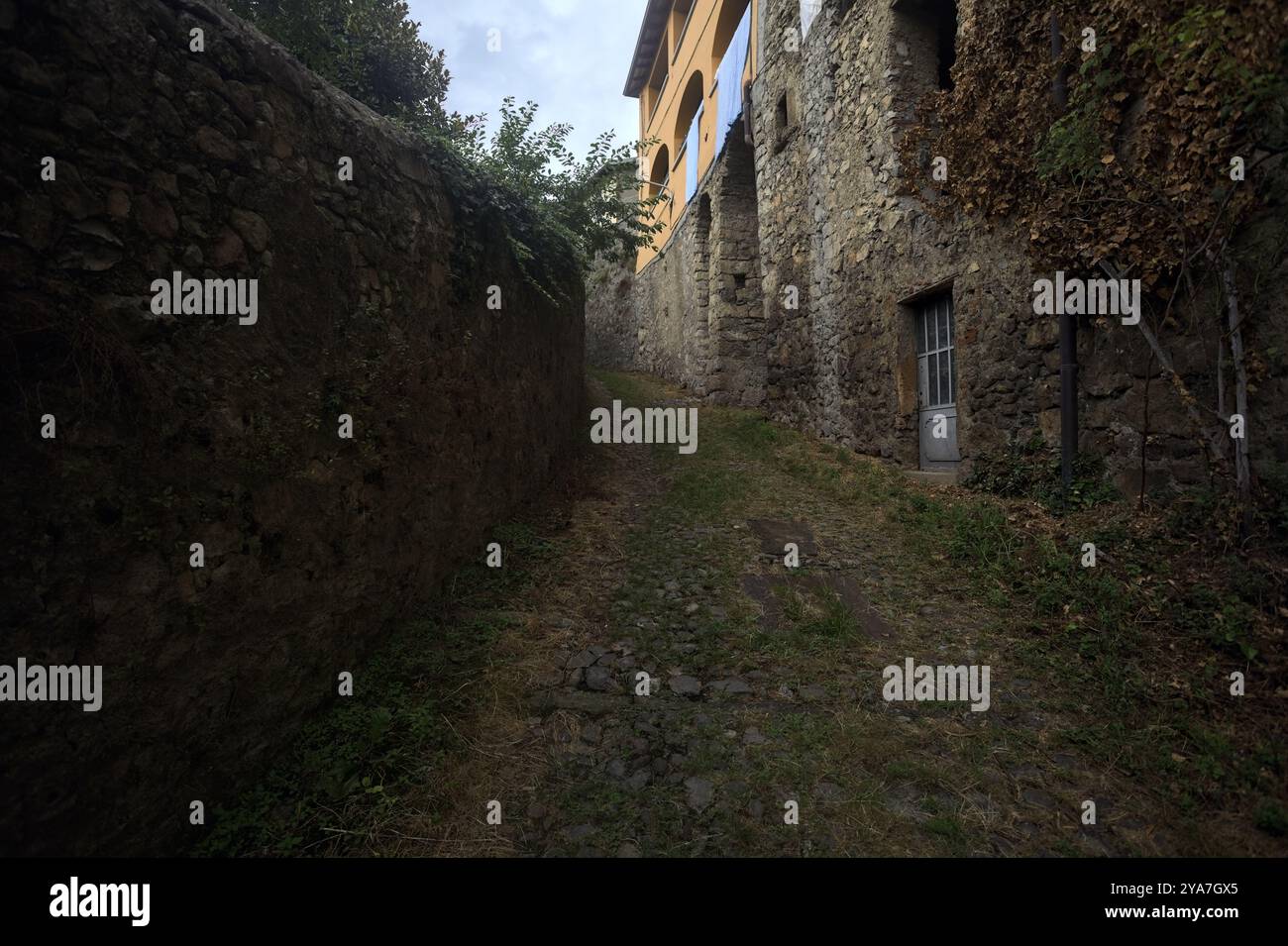 Schlampiger Kopfsteinpflasterweg zwischen einer Steinmauer und einem Steingebäude in den Bergen Stockfoto